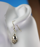 Silver skull-shaped earring on a white mannequin ear with a blue background